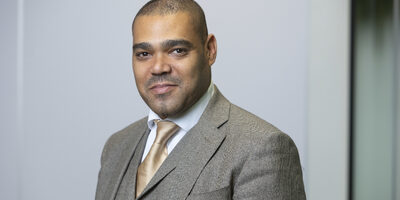 Man in brown suit smiling at camera.